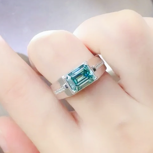 Silver ring with a green gemstone on a hand against a neutral background