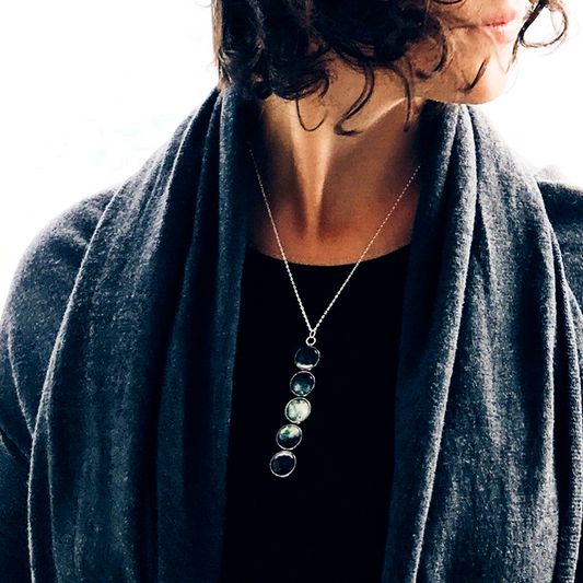Person wearing a dark gray sweater with a necklace featuring three circular pendants.