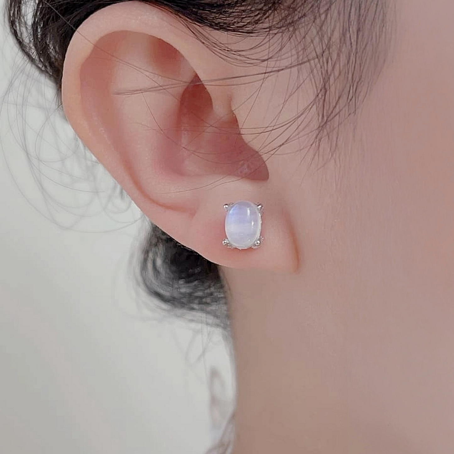Close-up of an ear wearing a silver earring with a gemstone on a neutral background
