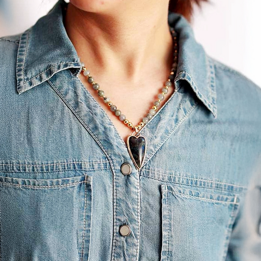 Person wearing a denim shirt with a necklace featuring a heart-shaped pendant.