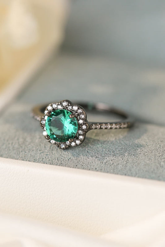 Hand-held close-up of a Paraiba-blue zircon halo ring in black gold–plated sterling with pavé band.