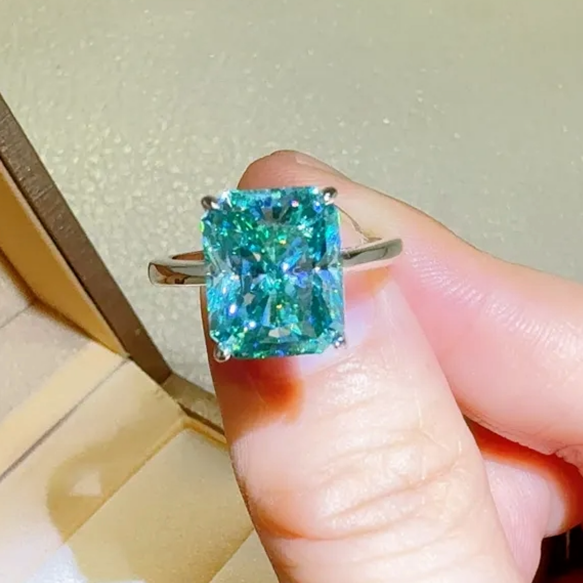 Hand holding a ring with a large green gemstone against a neutral background