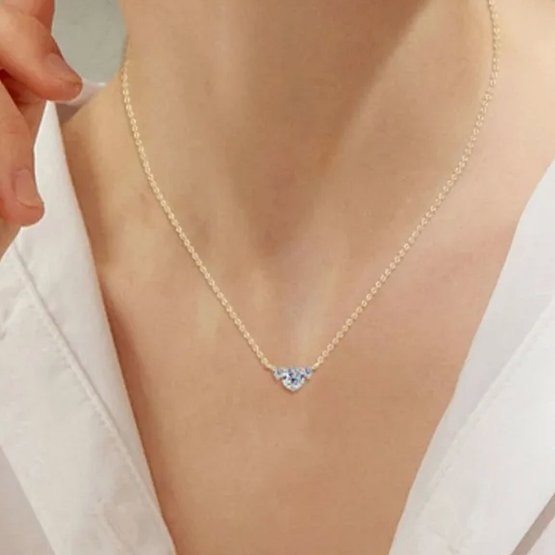 Gold necklace with a heart-shaped blue gemstone on a person wearing a white top.