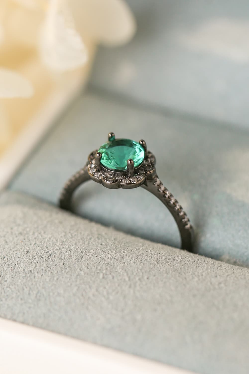 Hand-held close-up of a Paraiba-blue zircon halo ring in black gold–plated sterling with pavé band.