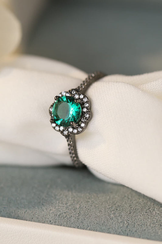 Hand-held close-up of a Paraiba-blue zircon halo ring in black gold–plated sterling with pavé band.