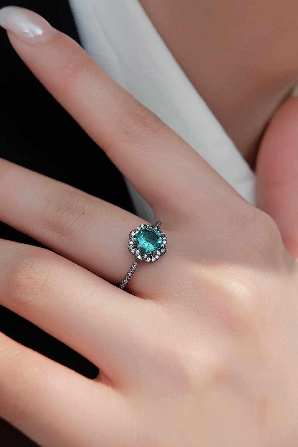 Hand-held close-up of a Paraiba-blue zircon halo ring in black gold–plated sterling with pavé band.
