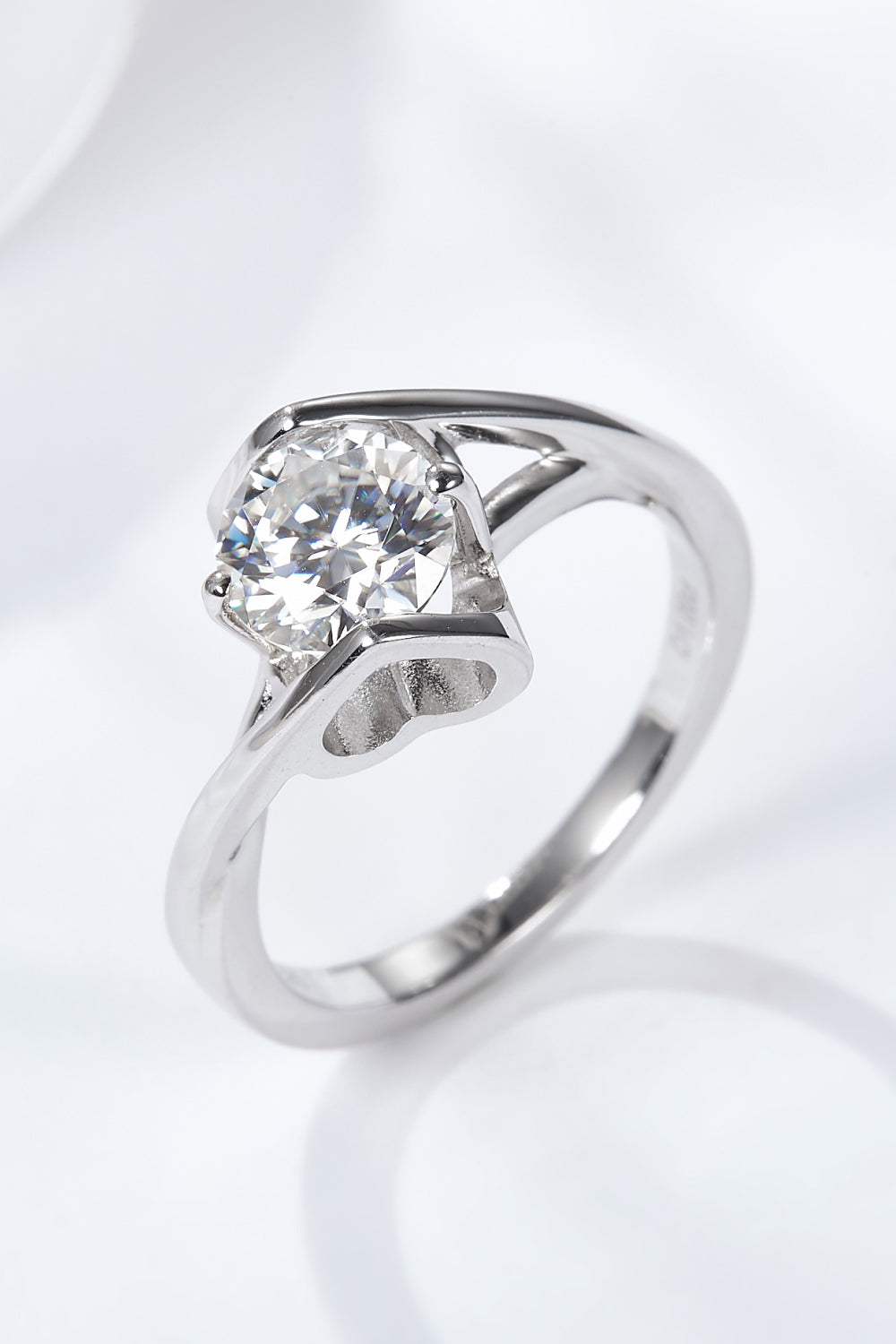 Three-quarter close-up of a 1 ct round-cut moissanite solitaire ring in platinum-plated sterling on black satin, showing facets and a slim band