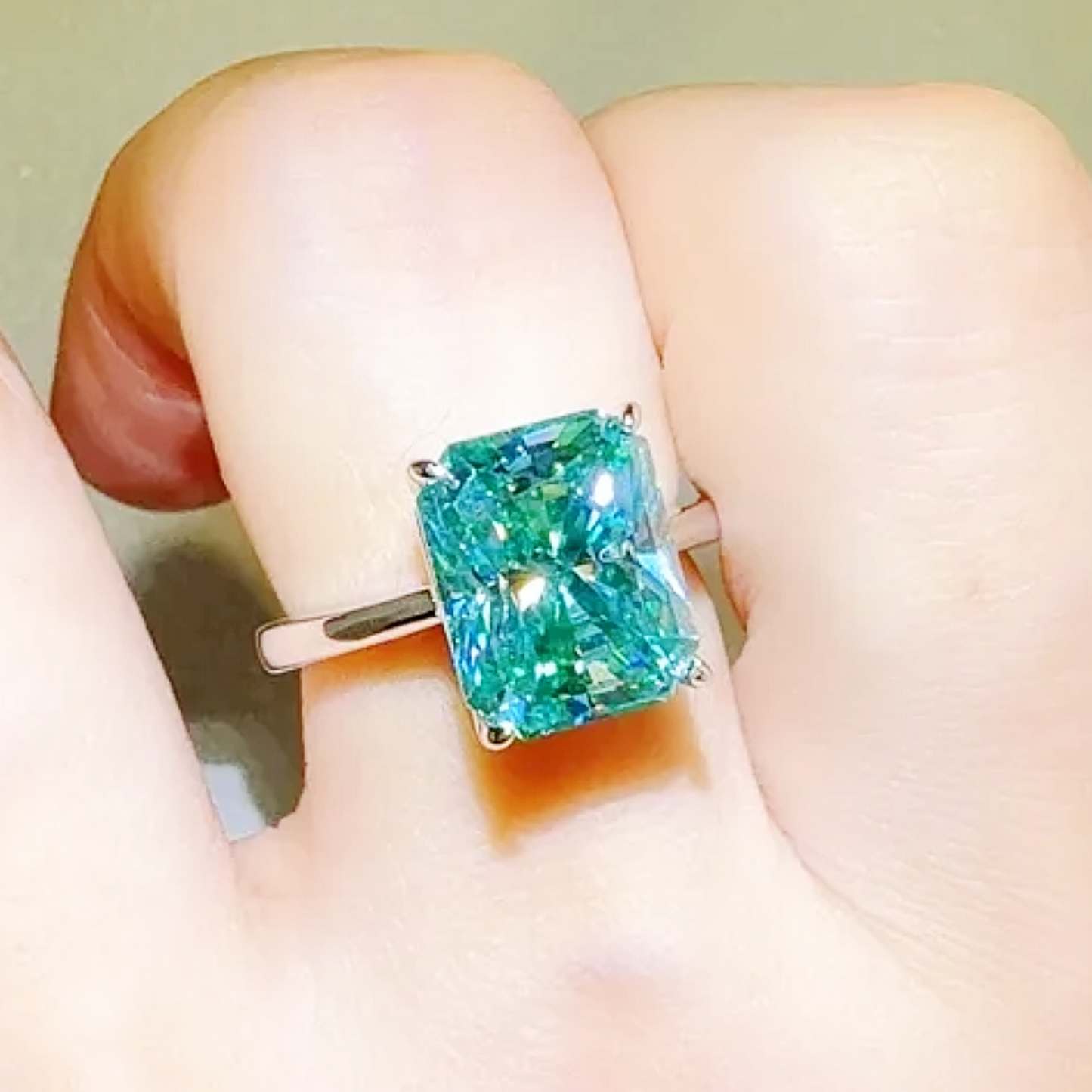 Ring with a large green gemstone held in a hand against a neutral background