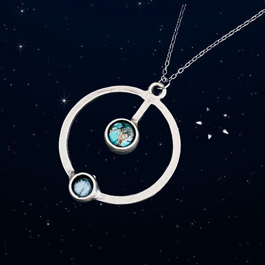 Silver necklace with circular pendant featuring two turquoise stones against a starry night sky background