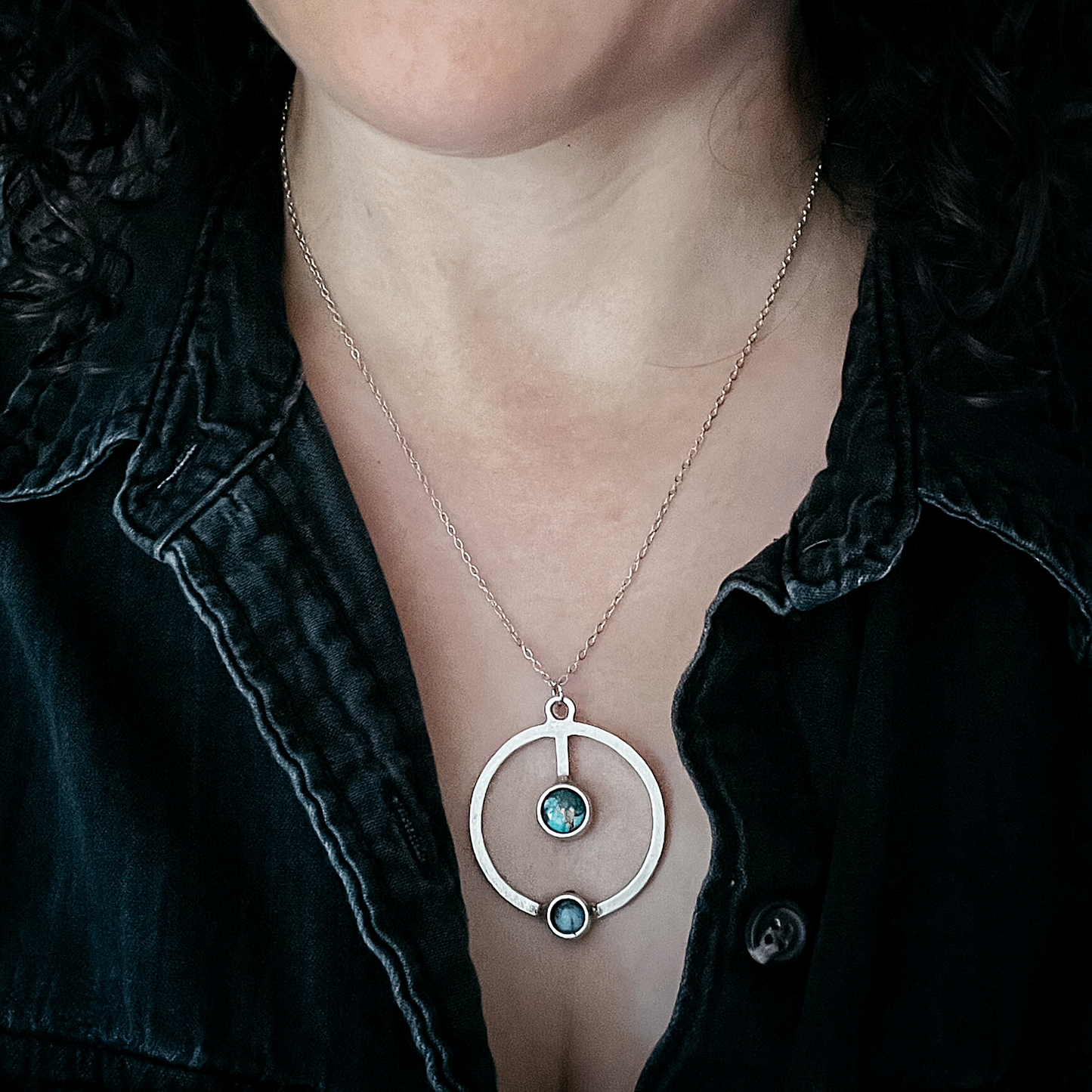 Necklace with a circular pendant featuring three small stones worn by a person.