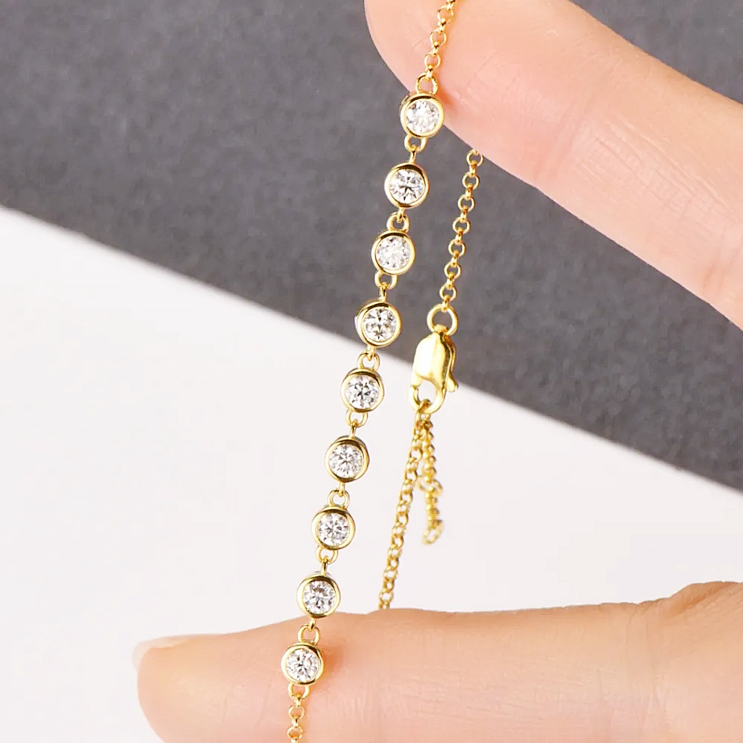 Gold chain bracelet with clear beads on a hand against a gray and white background