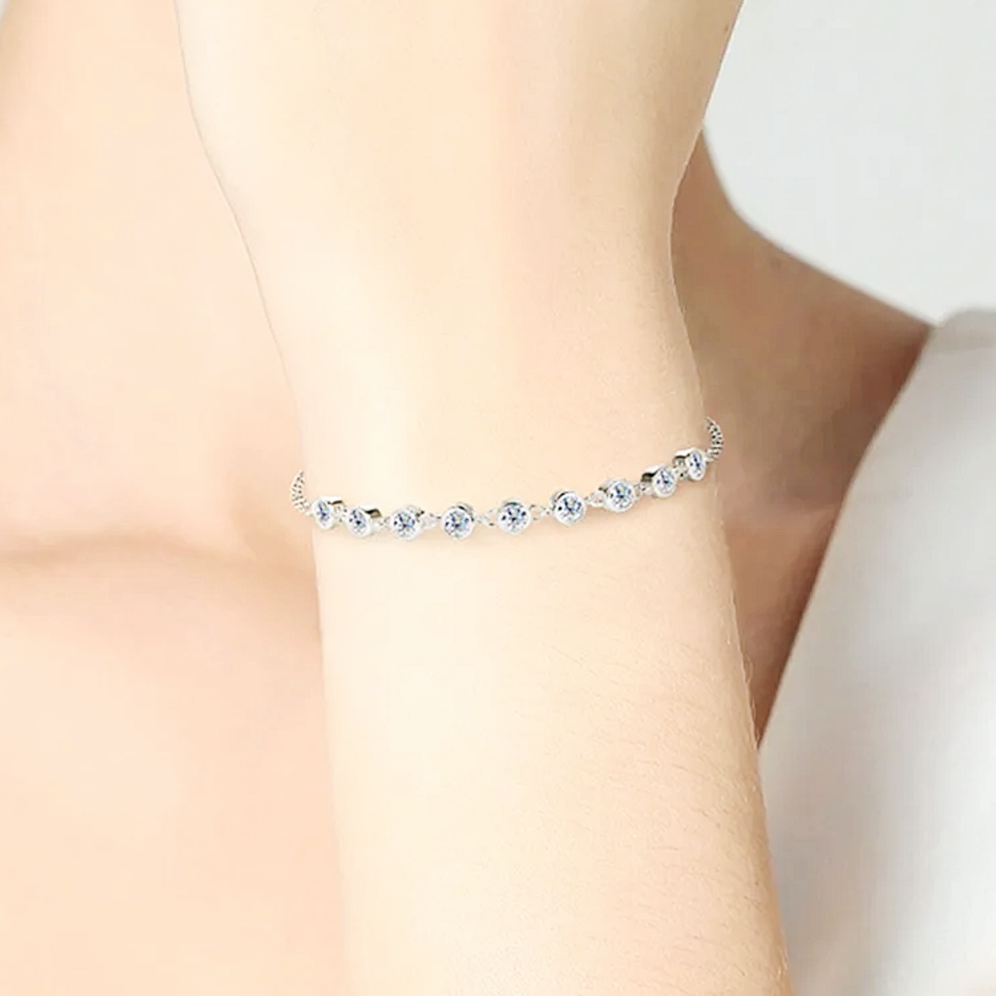 Silver anklet with clear stones on a person's ankle against a neutral background