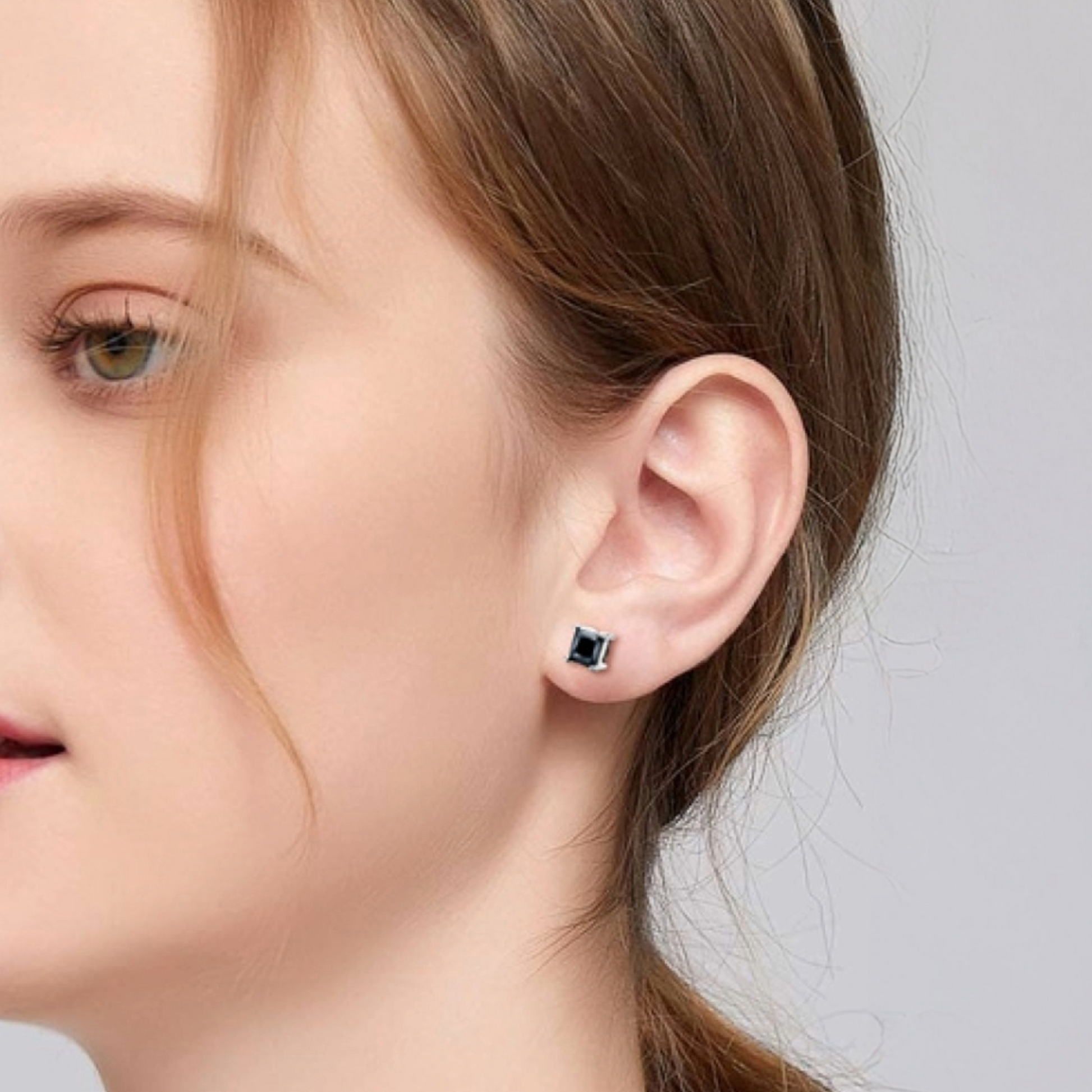 Close-up of a person wearing black stud earrings with a neutral background