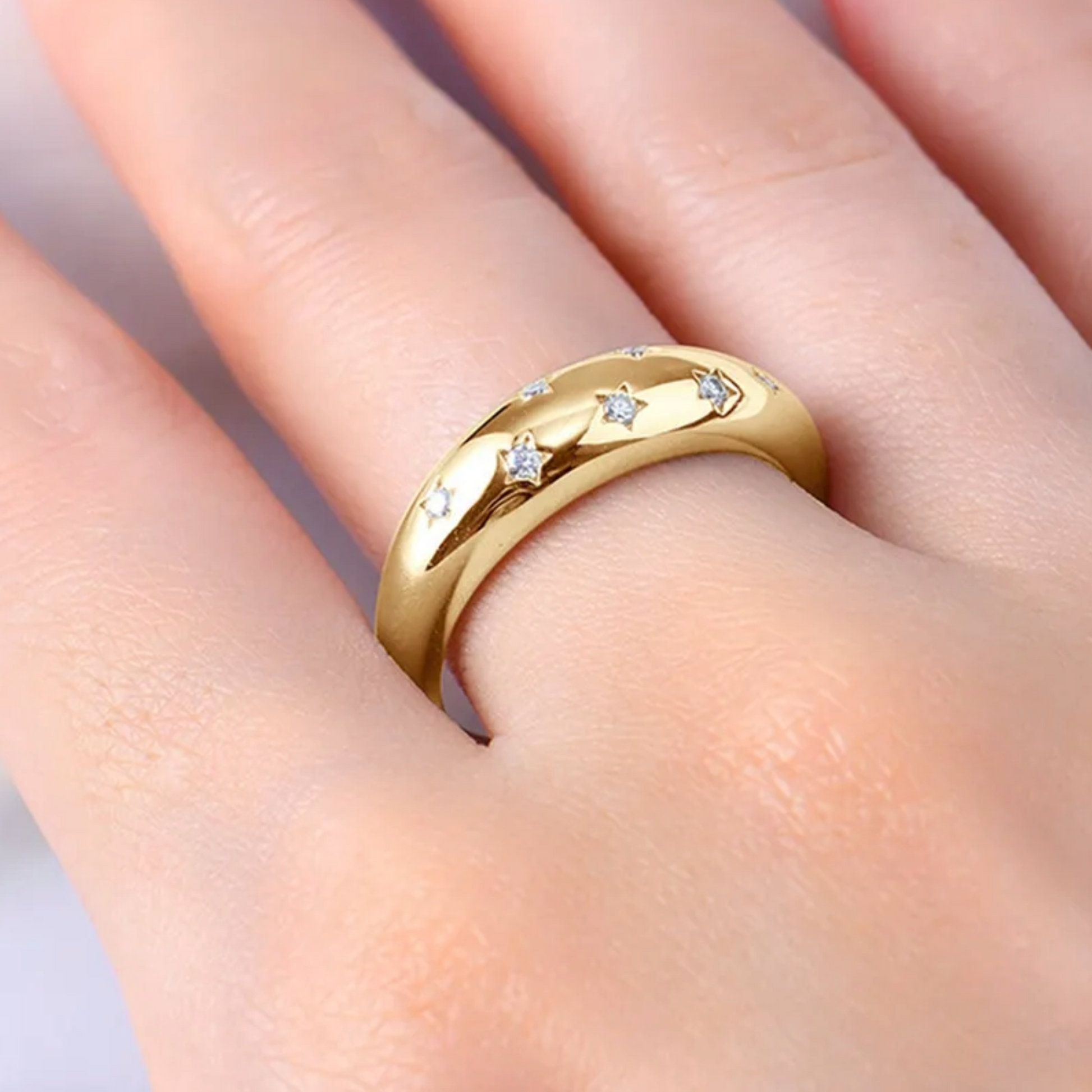 Gold ring with small diamonds on a finger against a neutral background