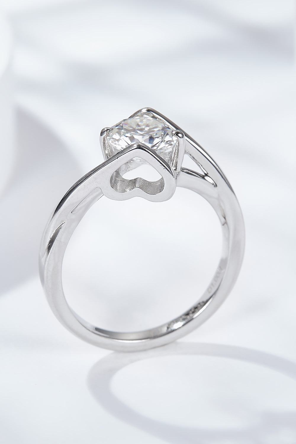 Top-down view of a 1 ct round moissanite solitaire ring on a white satin background, prong setting and slender band visible.