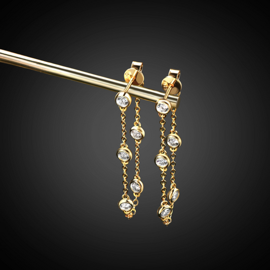 Gold earrings with chain and gemstone details on a black background