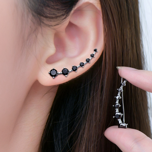 Close-up of an ear with black gemstone earrings being adjusted by a hand.