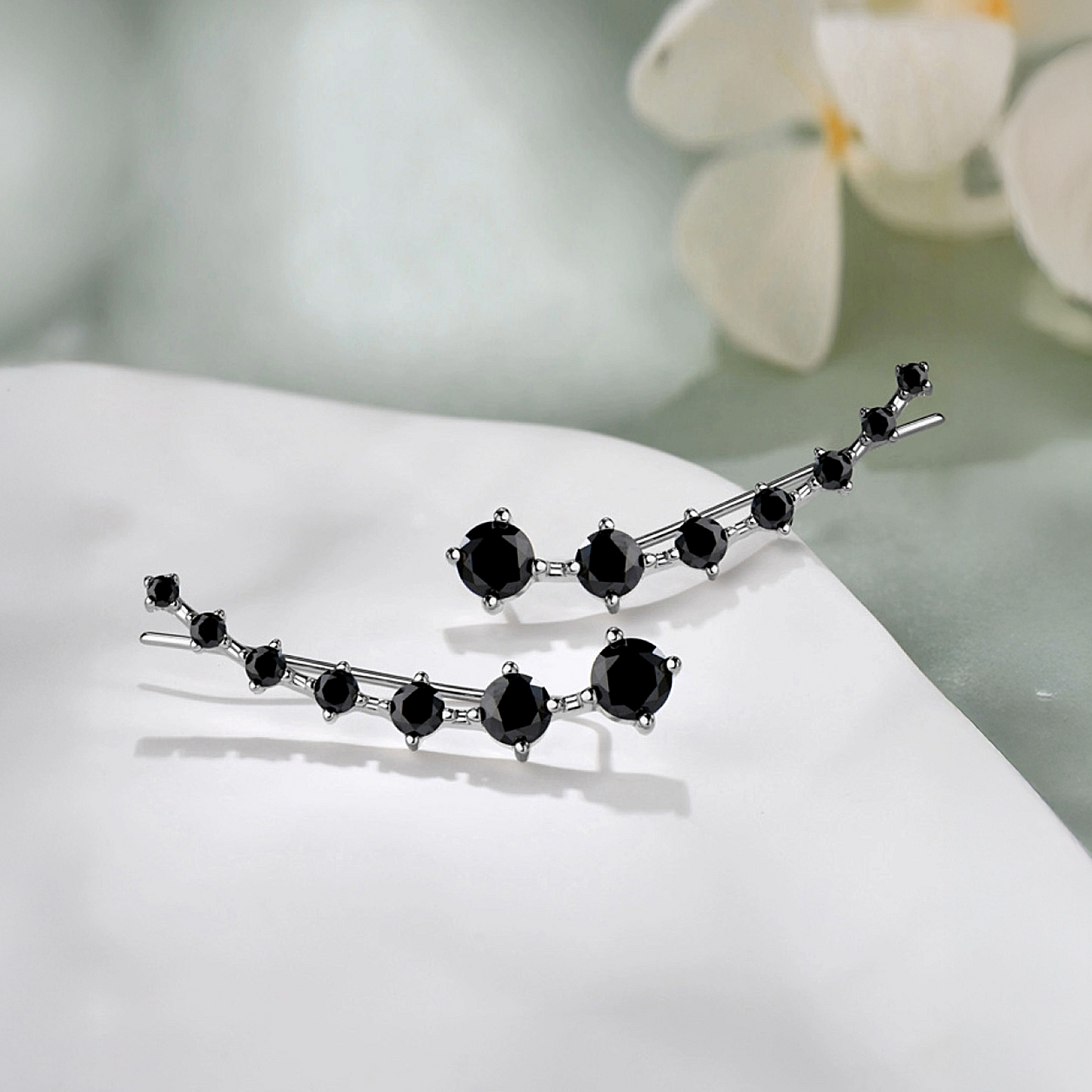 Pair of black gemstone earrings on a white surface with a blurred floral background
