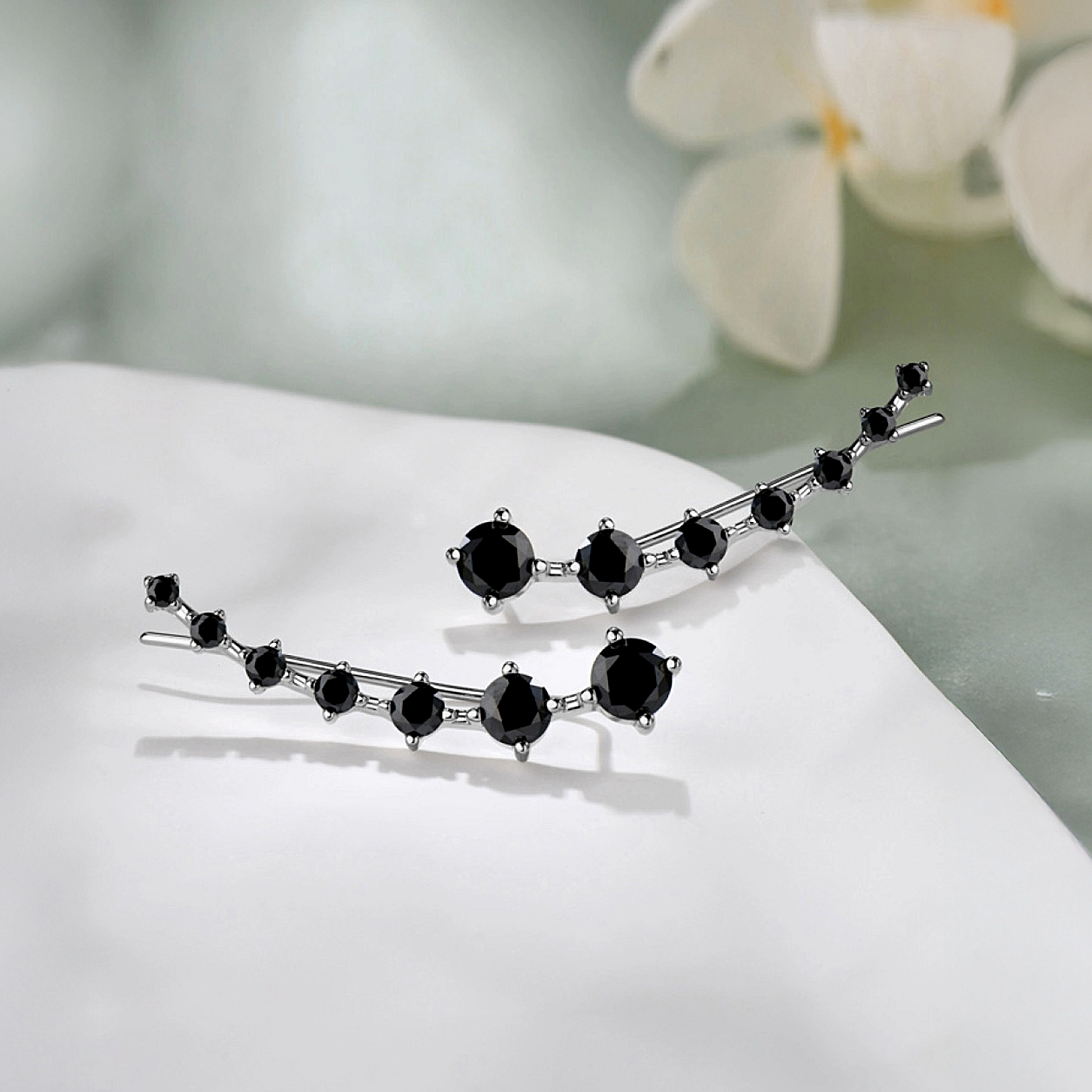 Pair of black gemstone earrings on a white surface with a blurred floral background