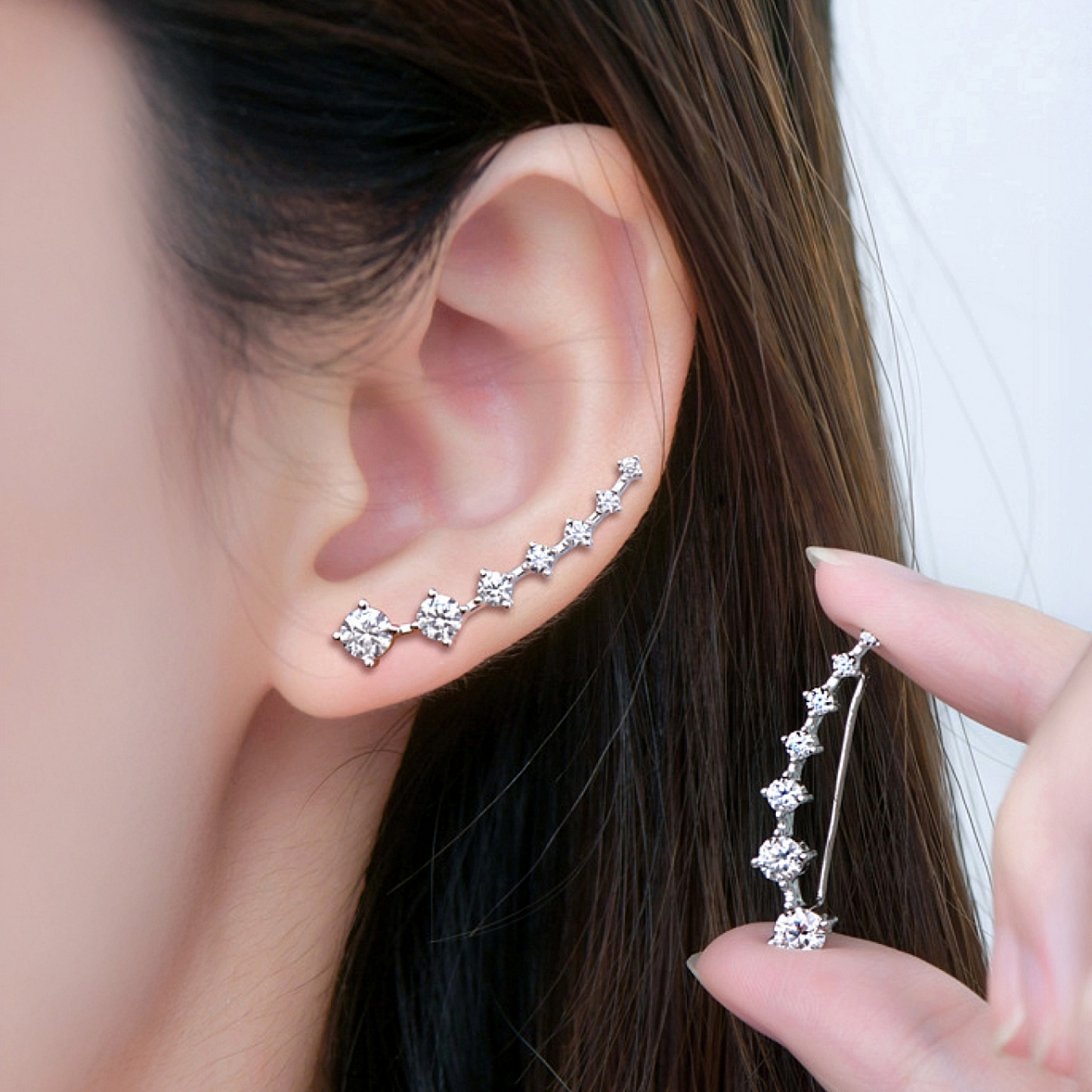 Close-up of a person wearing a silver earring with a hand holding another similar earring.