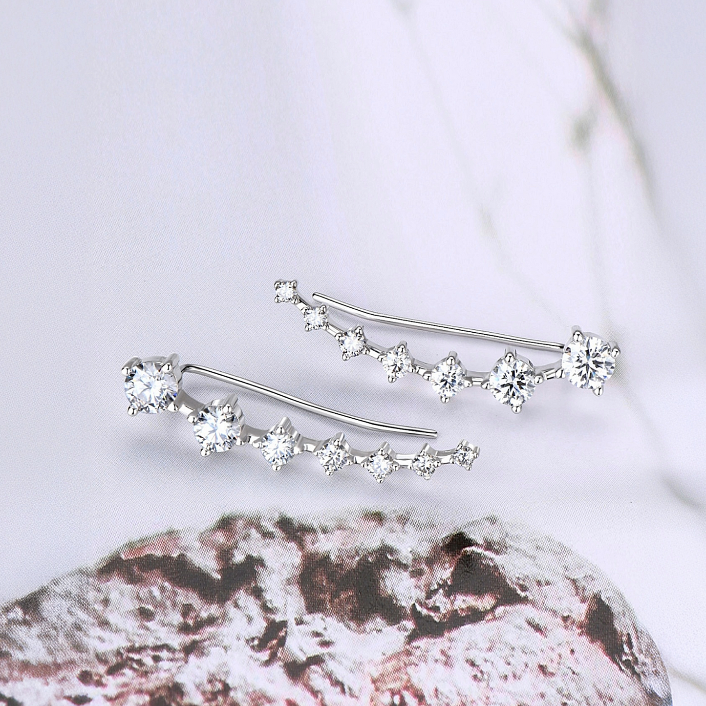 Silver earrings with clear gemstones on a textured surface