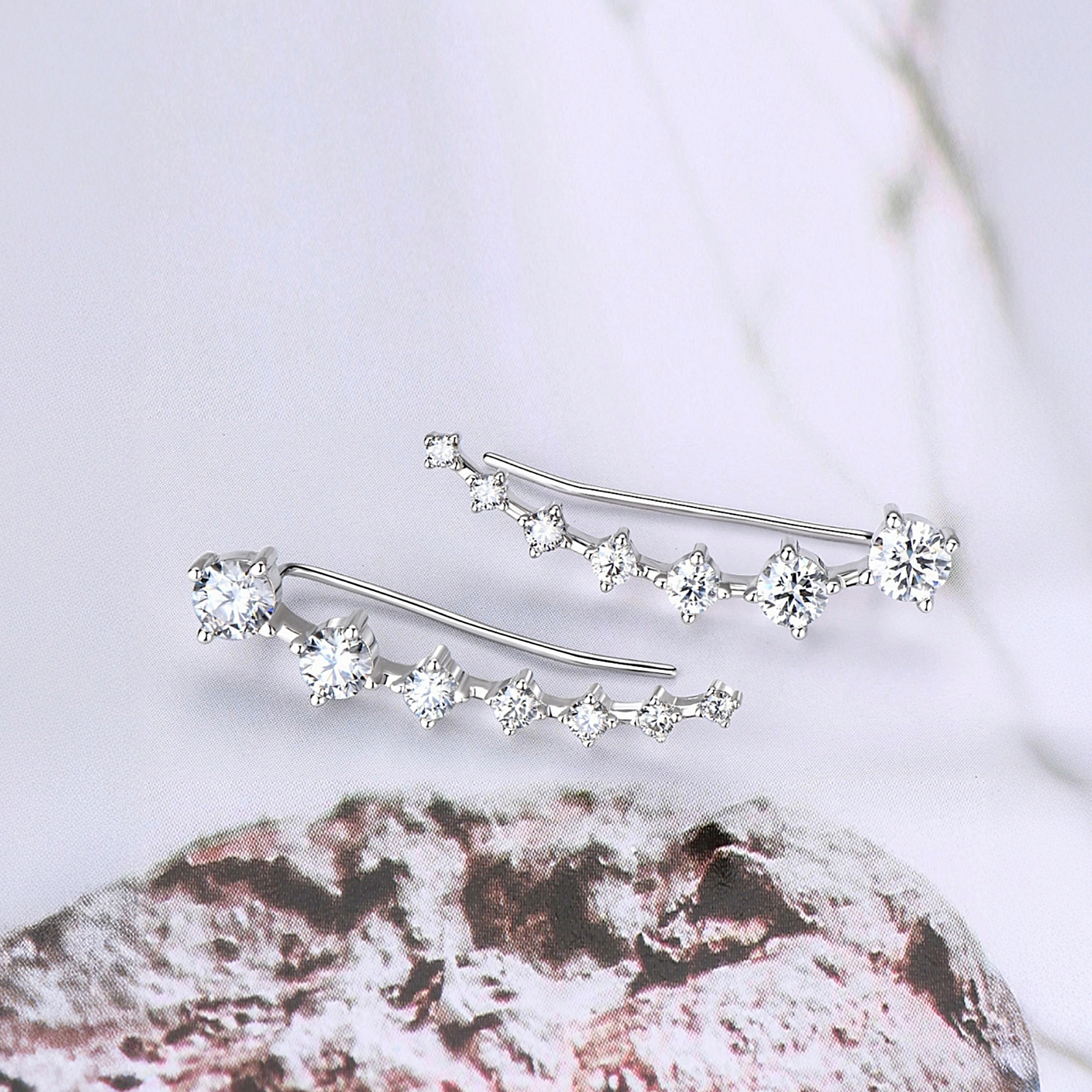 Silver earrings with clear gemstones on a textured surface