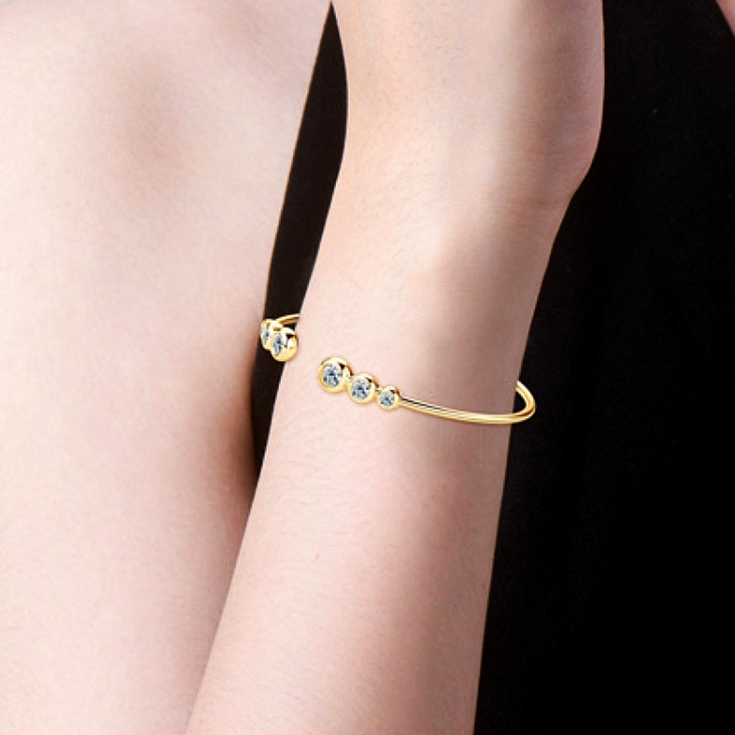 Gold bracelet with gemstones on a person's wrist against a black background