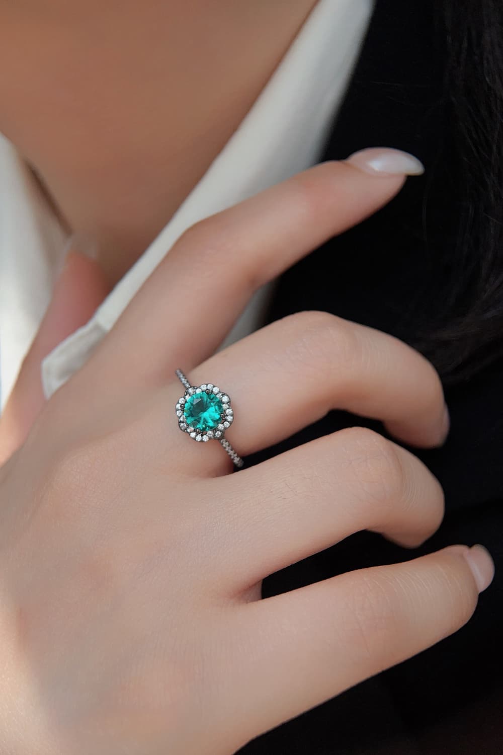 Hand-held close-up of a Paraiba-blue zircon halo ring in black gold–plated sterling with pavé band.