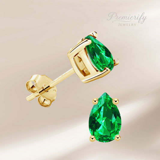 Gold earrings with green gemstones on a beige background