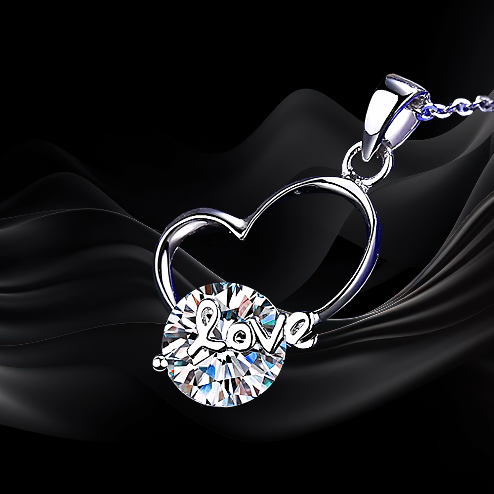 Silver heart-shaped necklace with a round 'LOVE' pendant on a black fabric background