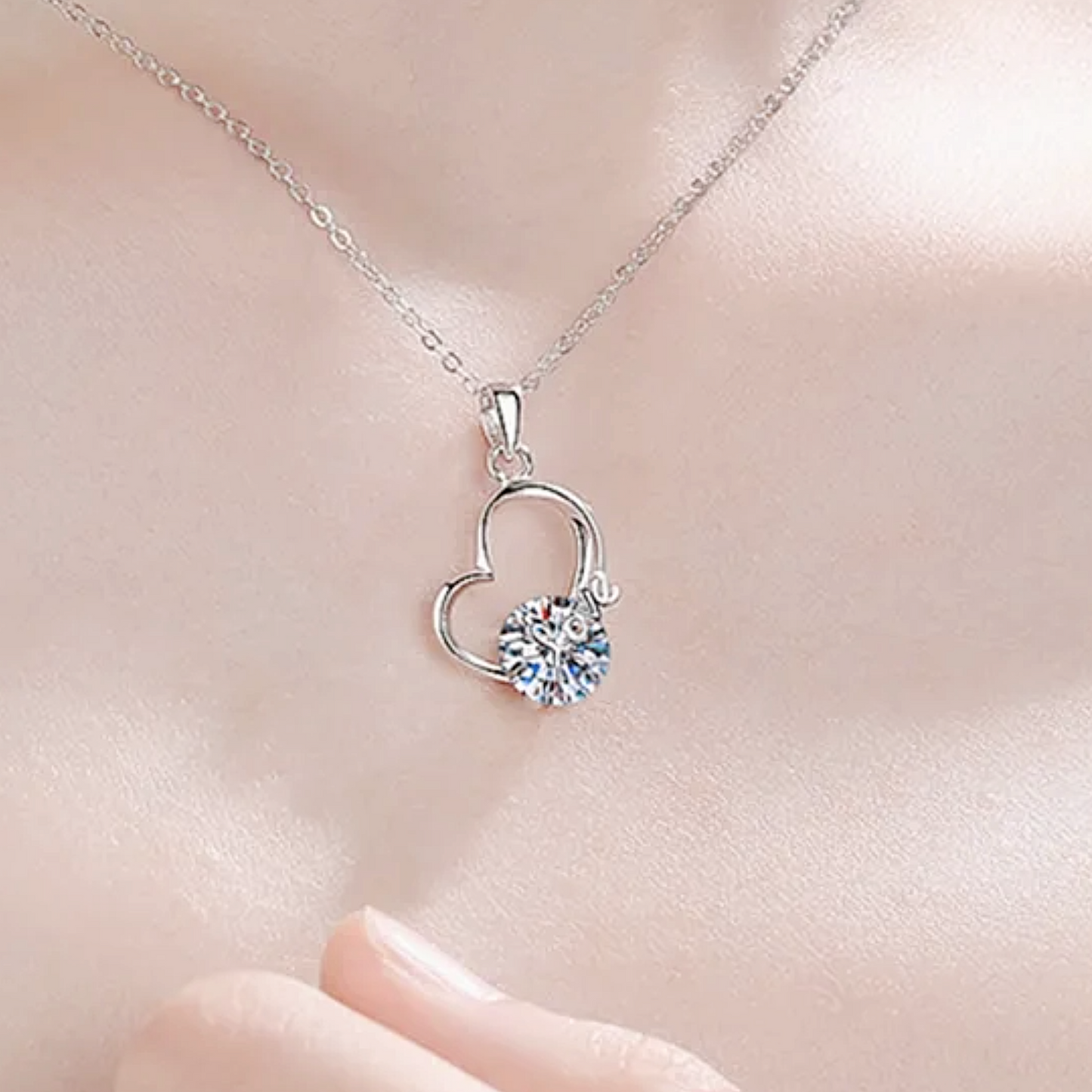 Silver heart-shaped necklace with a clear gemstone on a soft pink background