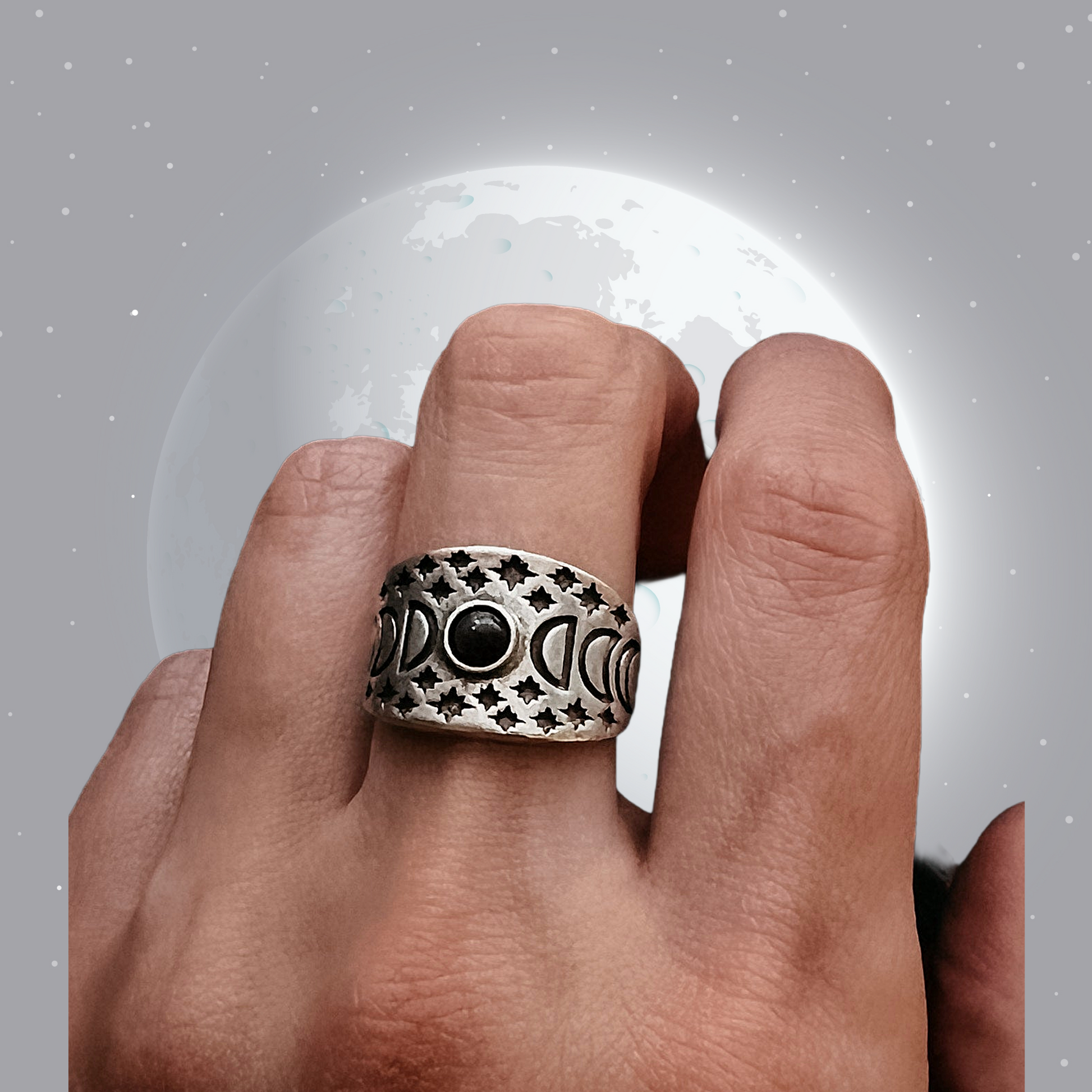 Hand wearing a silver ring with black stones against a gray background