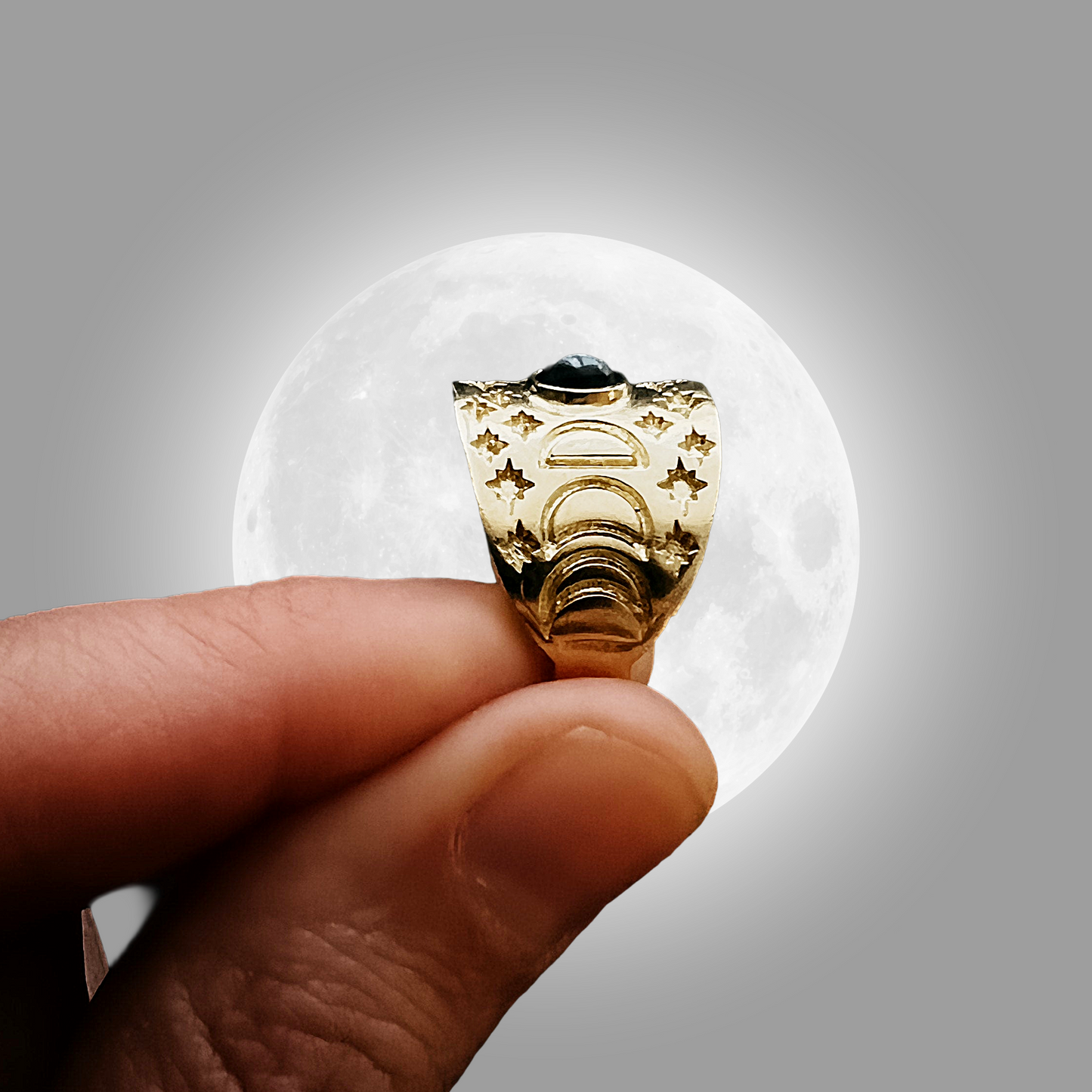 Gold ring with star design held between fingers against a gray background