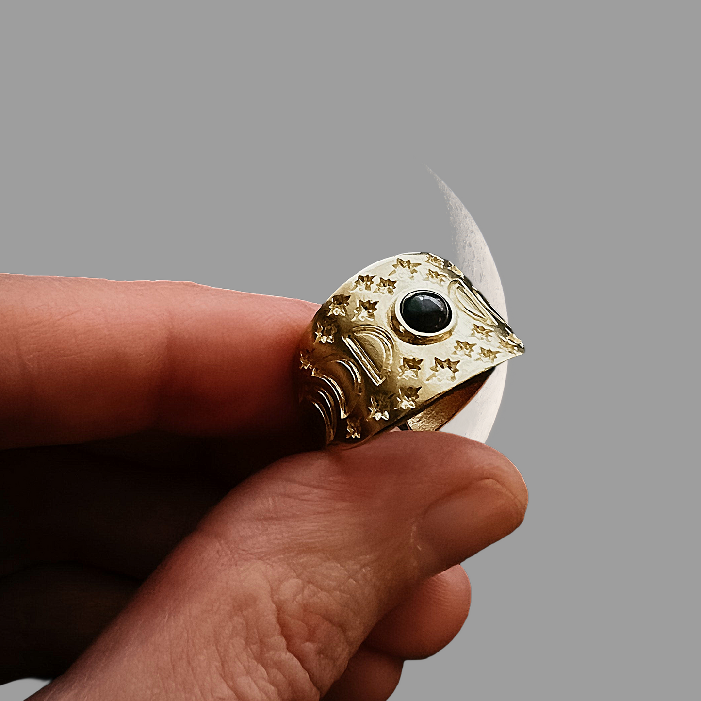 Hand holding a ring with decorative band against a gray background