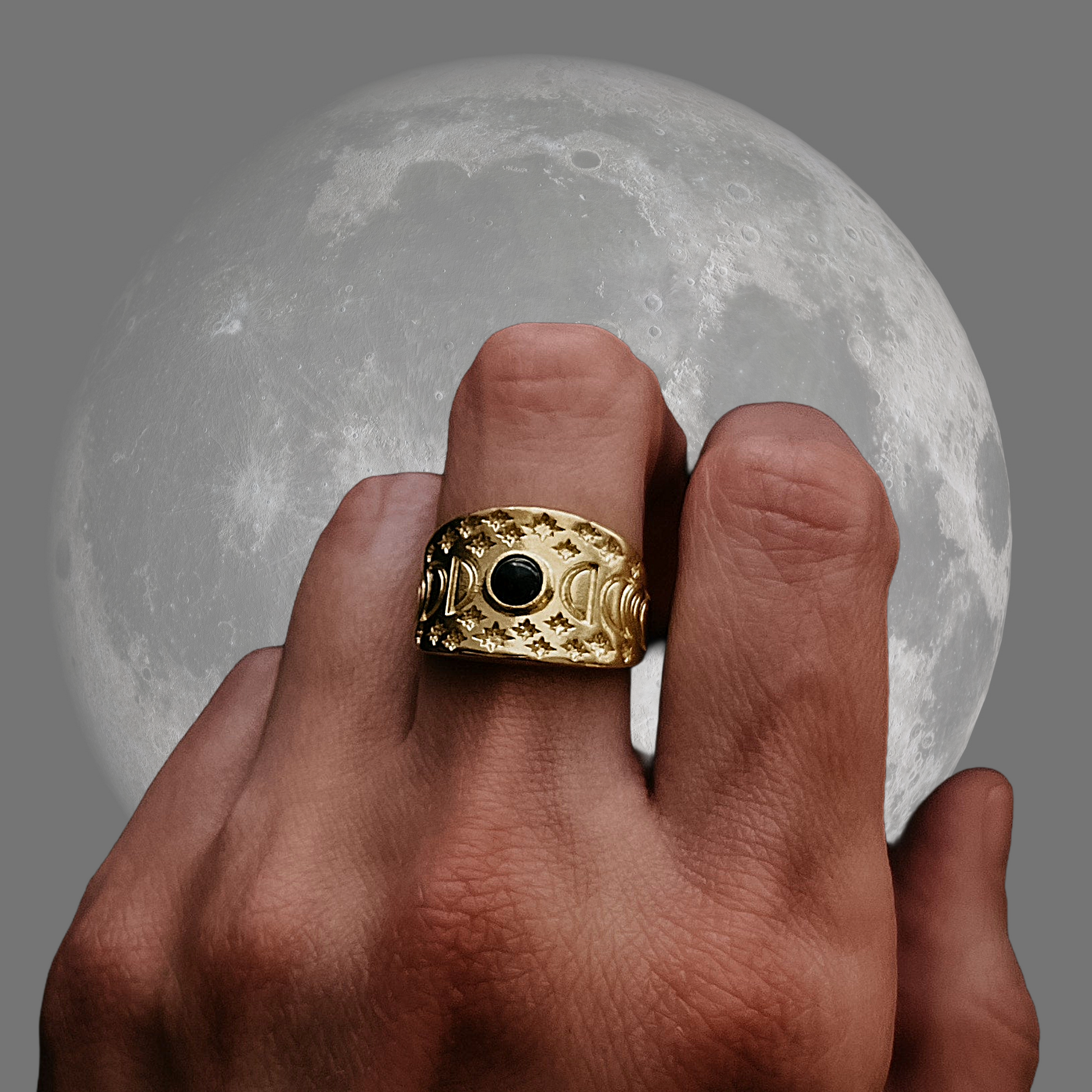 Gold ring with a black gemstone on a finger in front of a moonlit sky