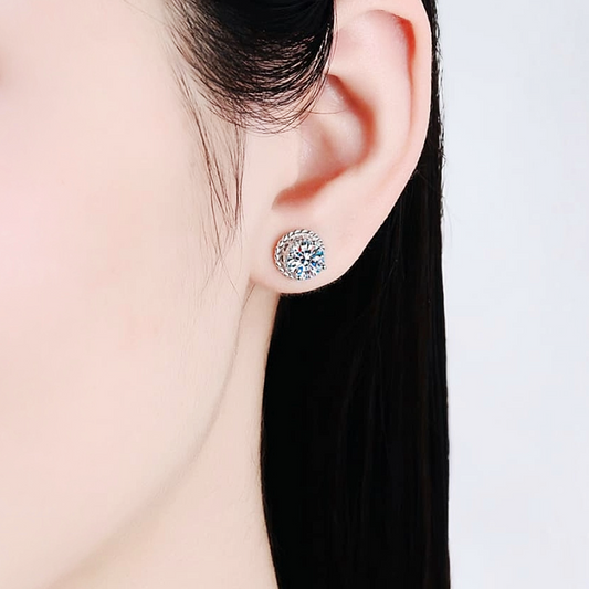 Close-up of an ear wearing a silver earring with a clear gemstone on a light background
