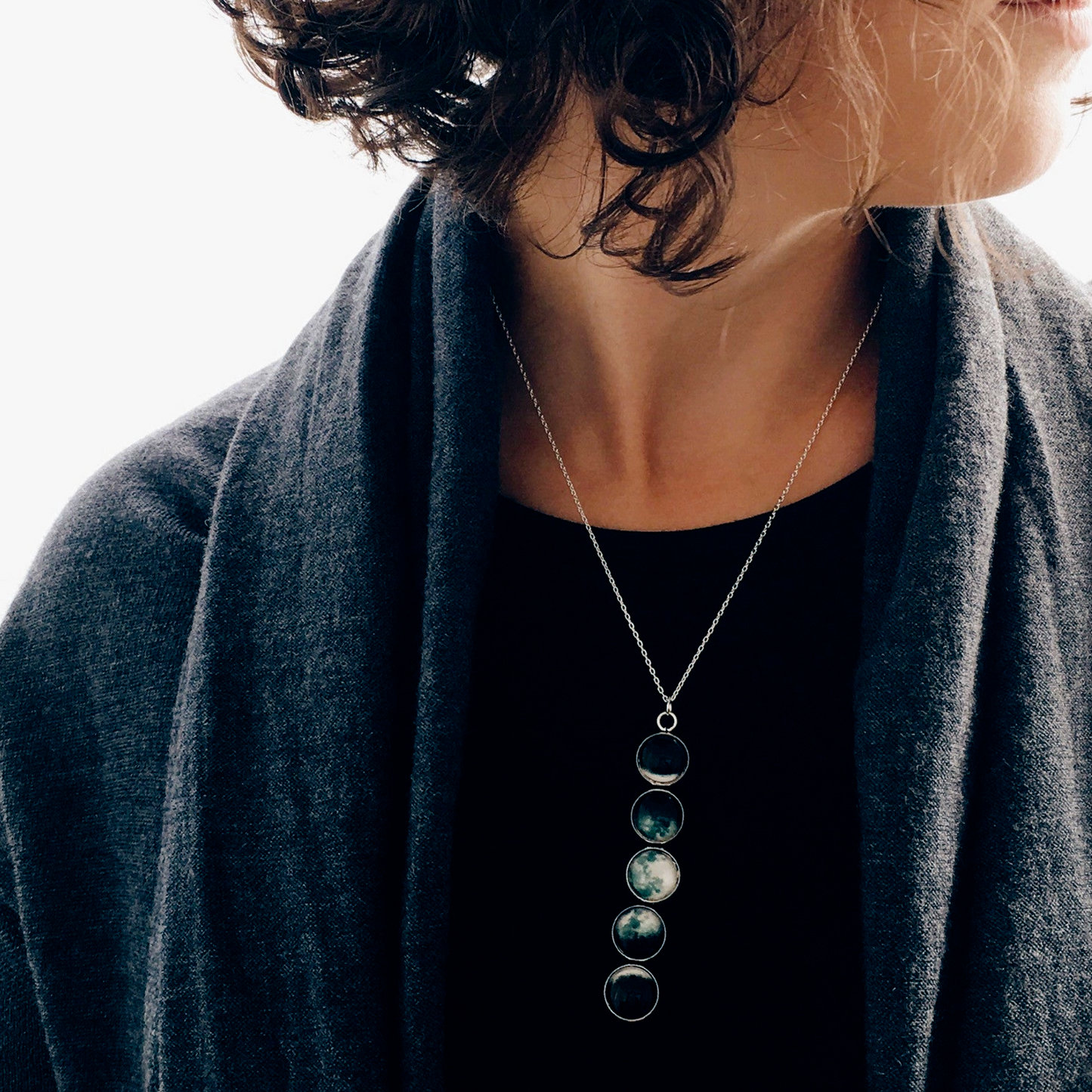 Person wearing a dark gray cardigan and black top with a necklace featuring three circular pendants.