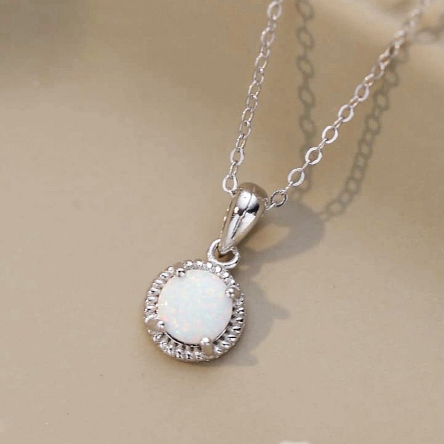Silver necklace with a round pendant featuring a white stone on a beige background