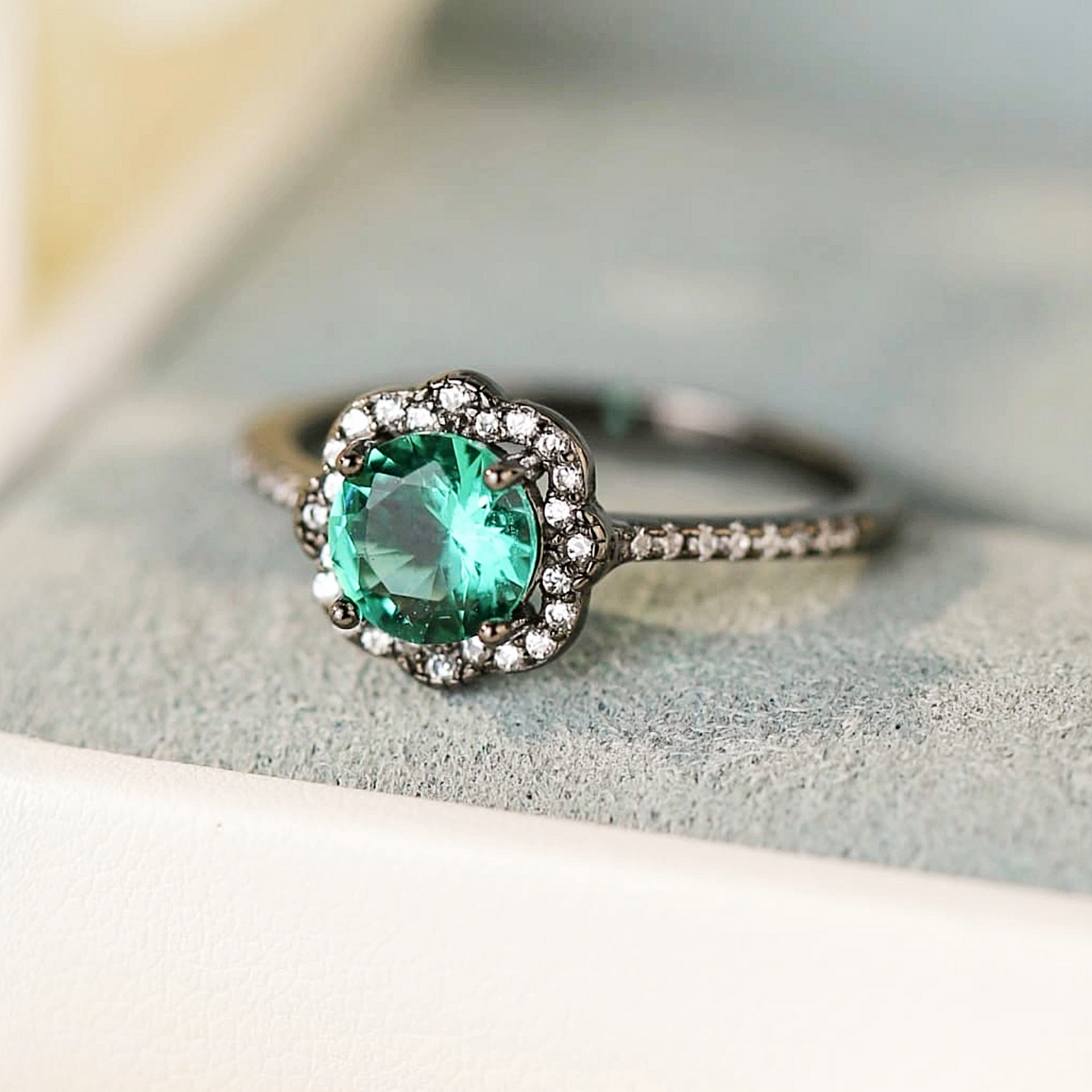 Close-up of Paraiba Noir™ ring with pavé halo, resting on soft cream fabric