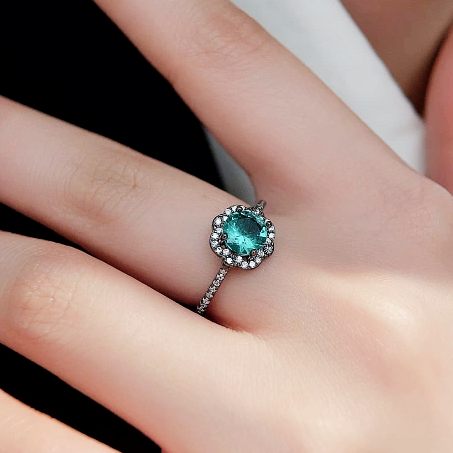 "Side view of Paraiba Noir™ ring worn on hand, showing black gold band and sparkling halo