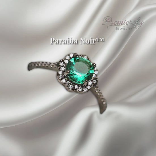 "Paraiba Noir™ ring with vivid blue zircon center on black gold band, displayed on silver satin fabric