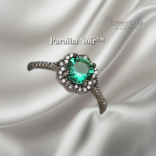 "Paraiba Noir™ ring with vivid blue zircon center on black gold band, displayed on silver satin fabric