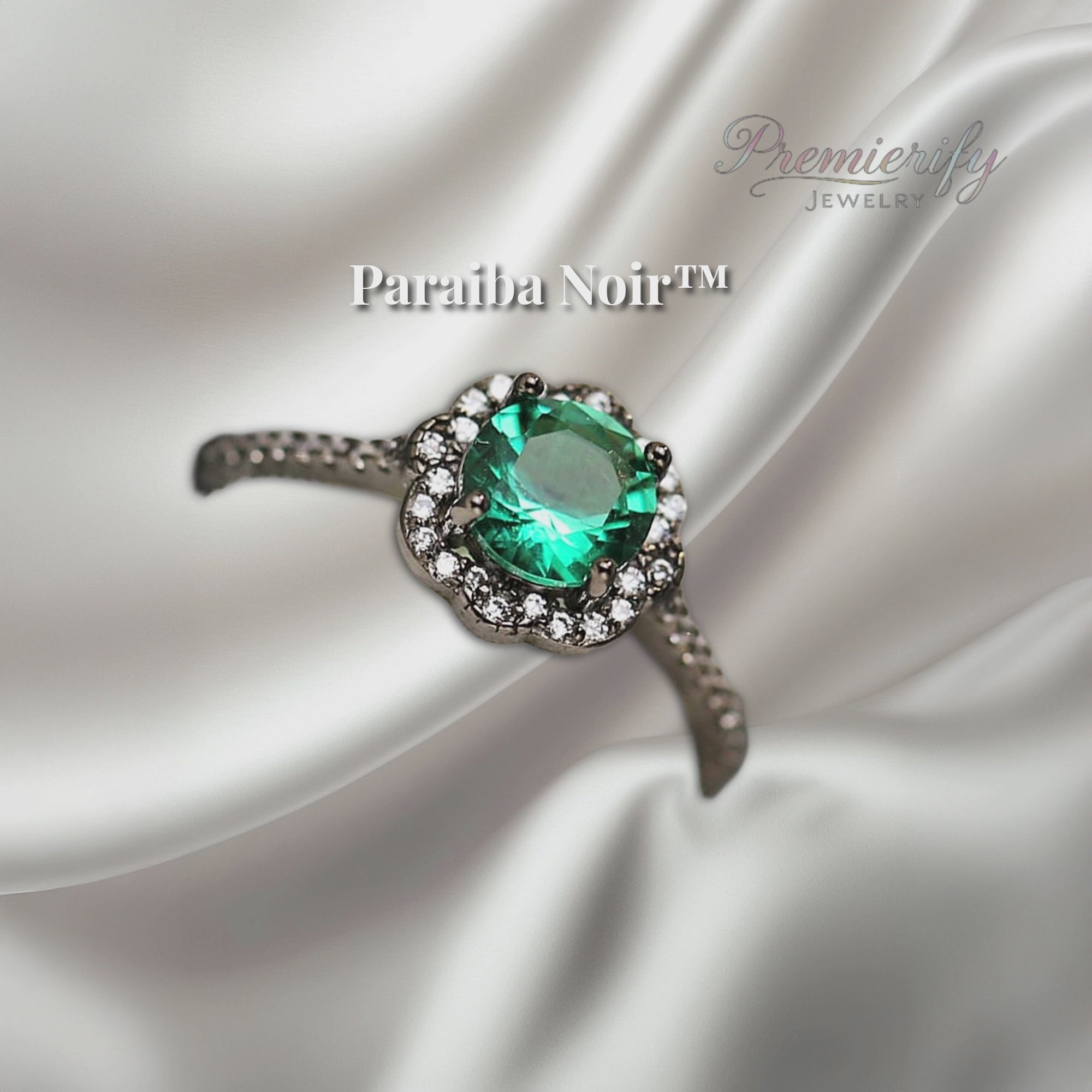 "Paraiba Noir™ ring with vivid blue zircon center on black gold band, displayed on silver satin fabric