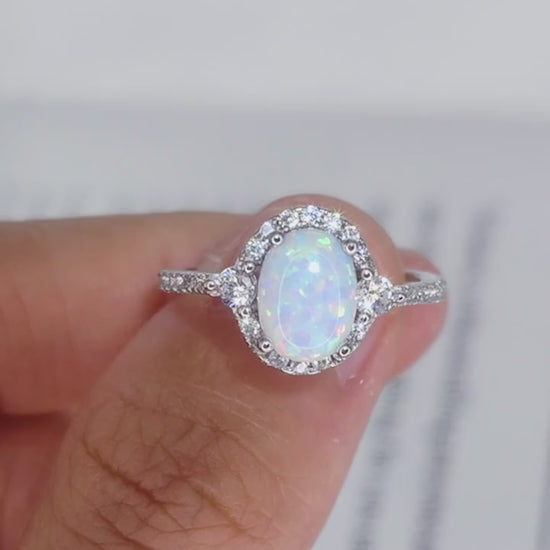 Short video of Iridesse™ oval opal halo ring in platinum-plated 925 silver, rotated in hand to show iridescent color play and sparkle
