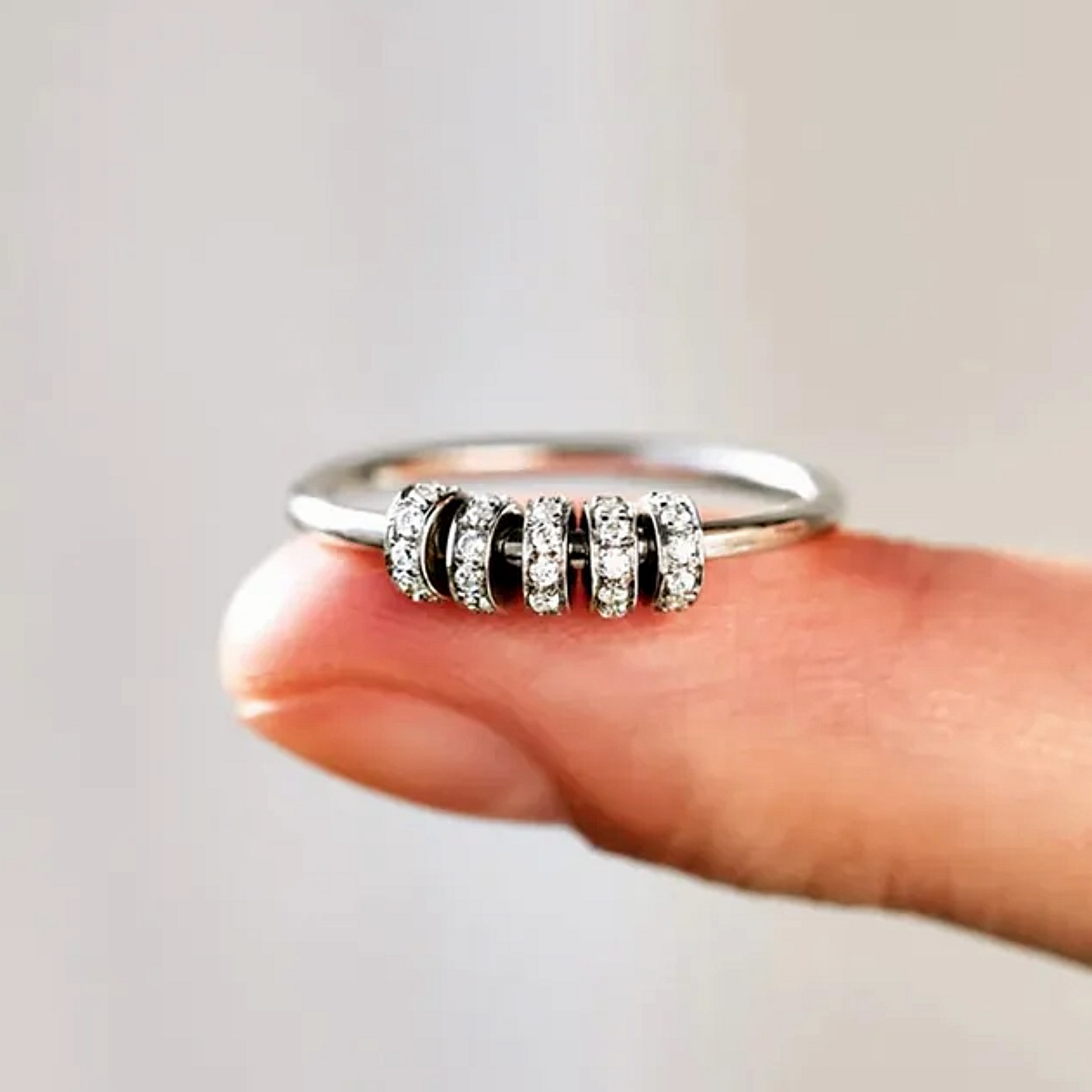 Silver ring with black and clear gemstones on a finger against a neutral background