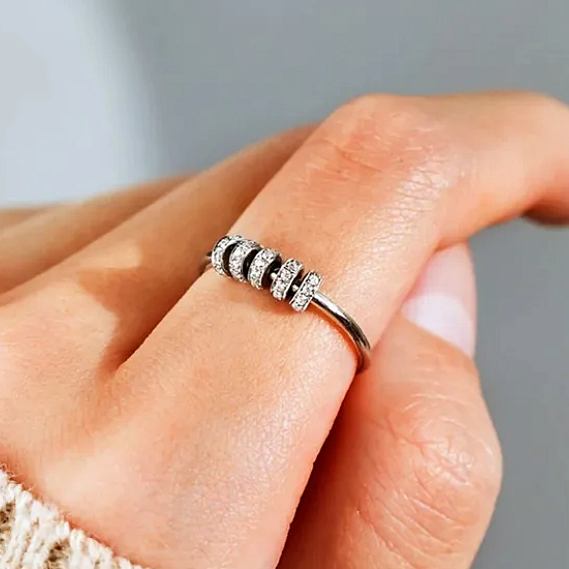 Silver ring with small stones on a person's finger against a neutral background
