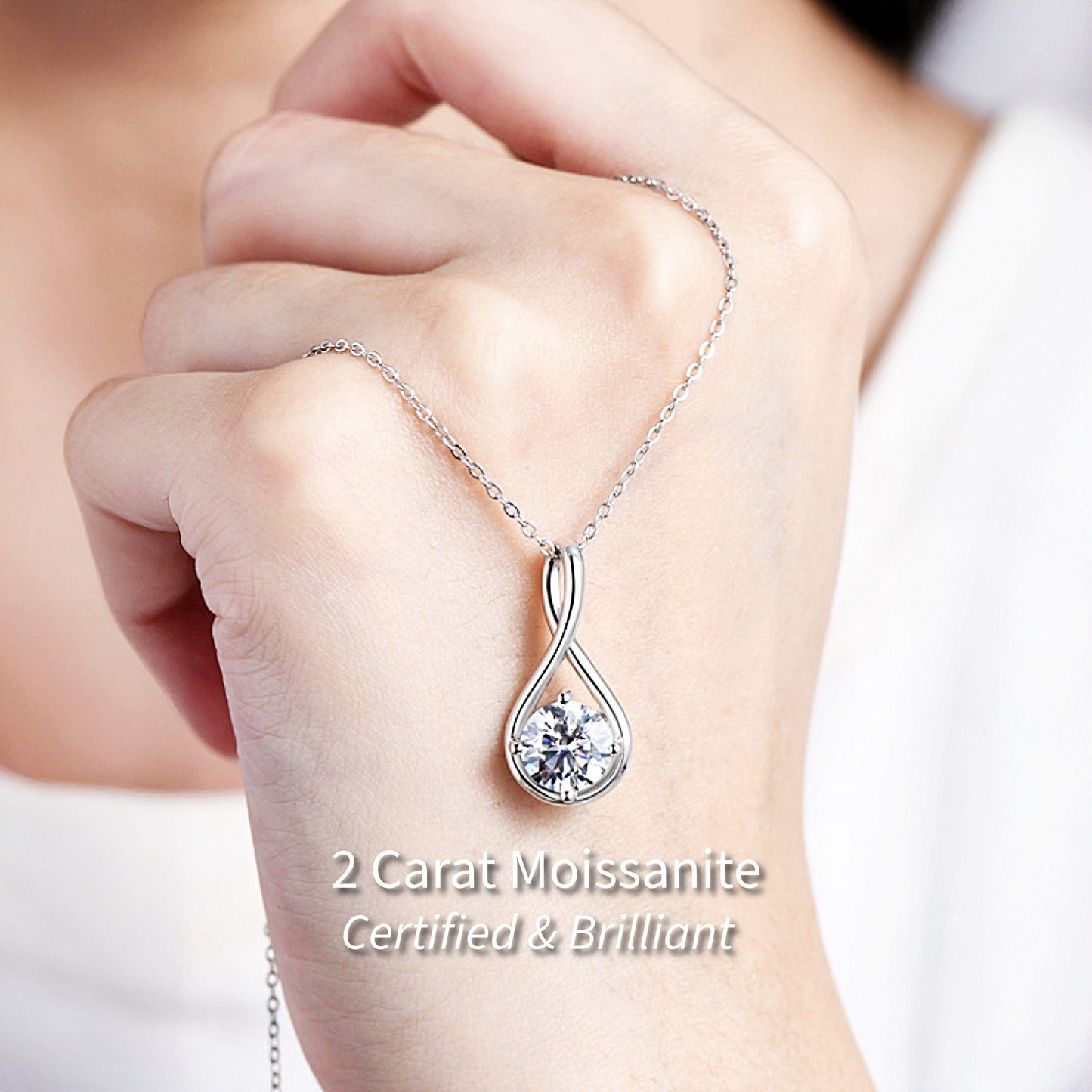 Persons hand holding silver infinity necklace certified and brilliant on light background.