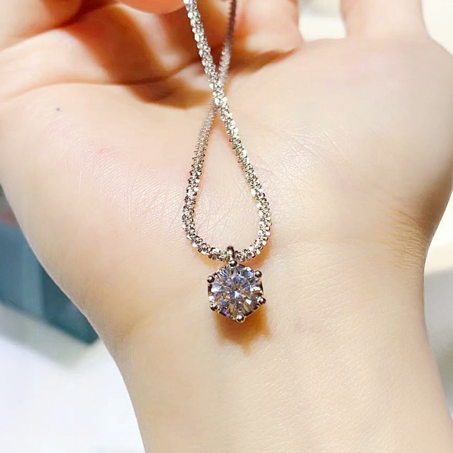 Silver necklace with a round pendant held by a hand against a neutral background