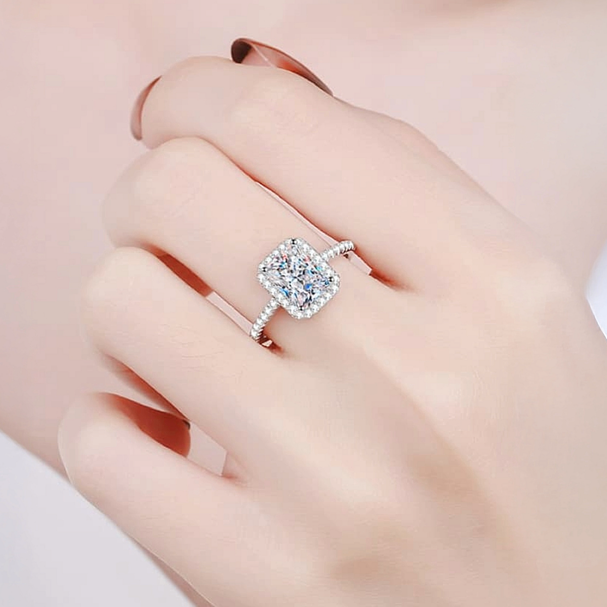Silver ring with a large diamond on a hand against a soft pink background